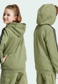 Sudadera verde de tela suave con un bolsillo frontal, capucha ajustable y franjas laterales negras. Textura lisa, corte relajado.