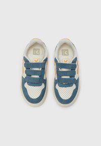 Modré semišové tenisky s bílými perforovanými koženými detaily, oranžovými prvky a pásky na suchý zip. Plochá gumová podrážka. Viditelné logo značky.