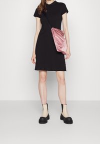 Robe polo noire à manches courtes, avec des détails de boutons. Associée à un sac à épaule en satin rose et des bottes à plateforme crème-noires.