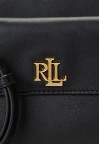 Mustassa nahkabagissa on kultainen "RL"-logo. Pinta on sileä, ompeleet näkyvät ja muotoilu on tyylikkään minimalistinen.
