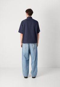 Marineblå t-skjorte med korte ermer og avslappet passform, kombinert med løse, lyseblå denimjeans, begge med minimalistisk design og uten synlige mønstre.