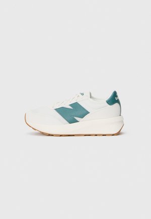 Weißer Sportschuh mit einem türkisen Streifen, strukturiertem Gewebe und einer Gummisohle. Abgerundete Silhouette mit gepolsterter Lasche und Schnürsenkeln.