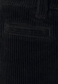 Svart kordflor tyg med vertikala ribbor, med en liten fickdetalj och en mjuk, texturerad yta.