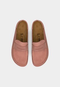 Ζευγάρι ροζ σουέντ μοκασίνια χωρίς κορδόνια με εμφανή ραφές και επενδυμένες καφέ πέλματα, εμφανίζονται από πάνω σε λευκό φόντο.