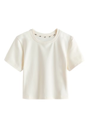 Woman standing indoors near stairs wearing cream-colored fitted leggings, matching cropped t-shirt, white socks, and silver sneakers.