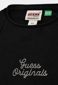 Zwarte sweatshirt met ronde halslijn, voorzien van "Guess Originals" in zilveren rhinestones. Eco-collectie label zichtbaar aan de binnenkant.