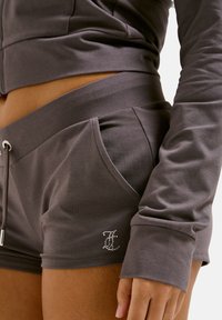 Gray loungewear set featuring a cropped long-sleeve top and shorts. The shorts have side pockets and a rhinestone logo accent. Smooth fabric.