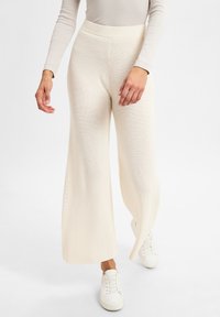 Weite, gestrickte Hosen in Off-White mit einem gerippten Bund und strukturiertem Stoff. Kombiniert mit weißen Sneakers.