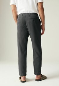 Pantalons légers gris avec une coupe décontractée, dotés de deux poches arrière et de détails de couture subtils. Associés à des chaussures à enfiler.