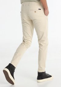 Chinos ajustés beiges en tissu lisse, dotés de poches arrière avec des détails en bouton et de poches latérales, associés à des baskets montantes noires.