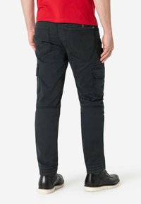 Schwarze Cargo-Hosen mit mehreren Taschen, tailliertem Design, genähten Details und elastischen Bündchen; kombiniert mit schwarzen Schuhen und einem roten Hemd.