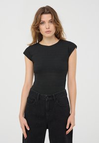 Top nero aderente con maniche corte a cuffia e texture a coste. Abbinato a jeans neri a vita alta con piccoli borchietti decorativi.