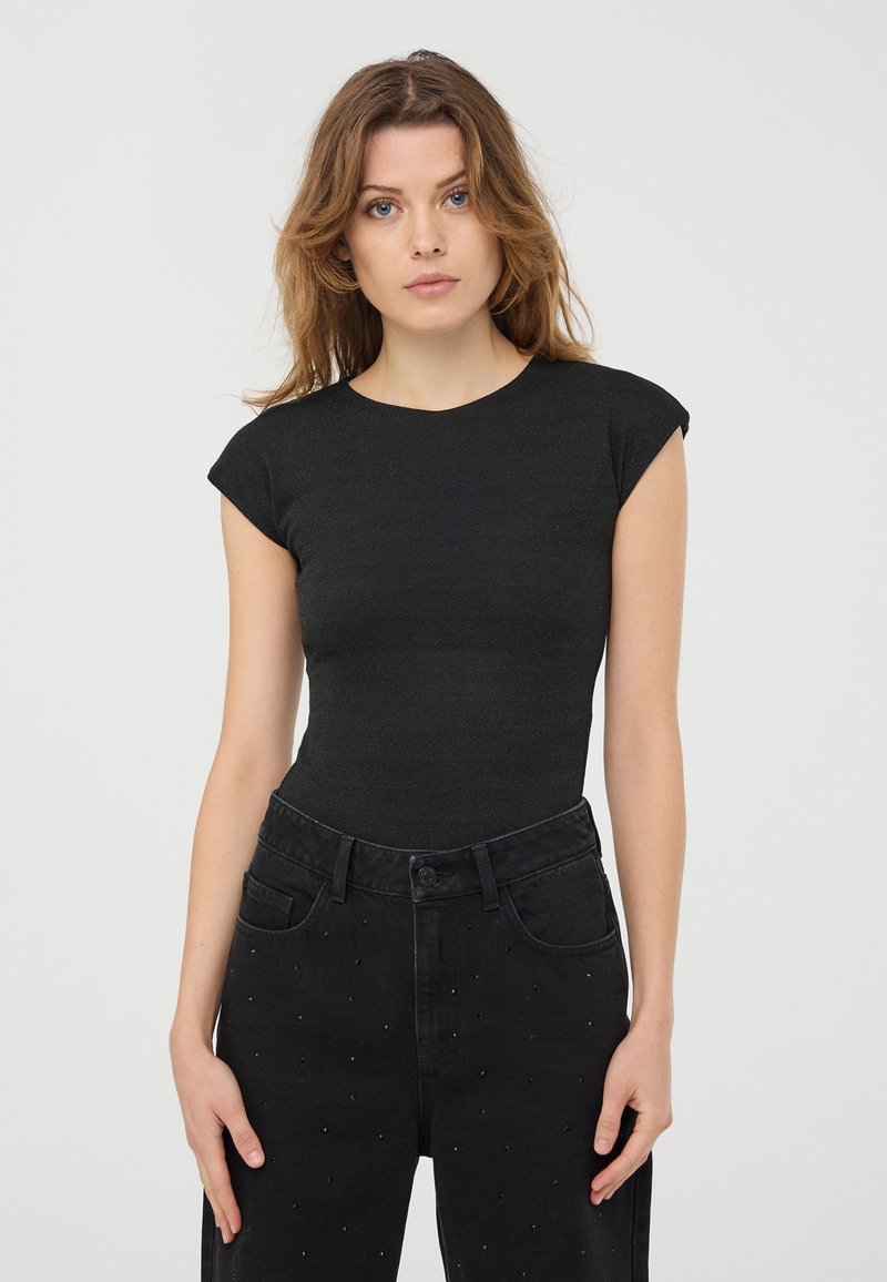 Top nero aderente con maniche corte a cuffia e texture a coste. Abbinato a jeans neri a vita alta con piccoli borchietti decorativi.