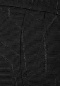 Tejido negro texturizado con patrones geométricos y un ligero brillo. Las costuras y los detalles de la confección son visibles, lo que realza el diseño general.