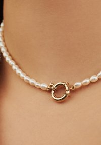 Collier de perles avec un fermoir circulaire en or, présentant une fine chaîne de perles blanches lustrées et une texture lisse et polie.