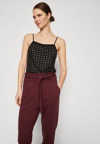Black sleeveless top with silver dot pattern, paired with burgundy high-waisted trousers featuring a tied belt and side pockets.