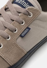 Grå canvas sneakers med bruna mockadetaljer, runda ögla och platta snören. Har en liten blå märkesetikett på sidan.