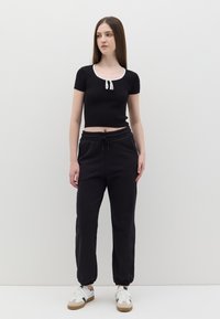 Top corto a righe nere con colletto bianco e dettaglio con fiocco, abbinato a pantaloni della tuta neri con vita elastica e orli a costina. Sneakers bianche con dettagli beige.