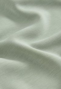 Tissu vert clair doux avec des plis lisses et une texture fine, montré en gros plan.