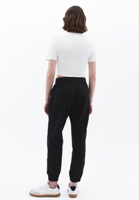 Witte getailleerde top met korte mouwen en zwarte sweatpants met elastische boorden. Witte sneakers met bruine zolen en donkere details. Schoon, minimalistisch ontwerp.