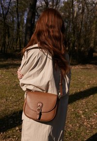 Brun læder crossover taske med en buet klap, prydet med en metalspænde og justerbar rem. Tekstureret overflade med en glat finish.