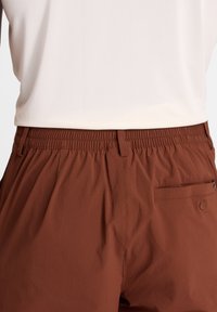 Pantaloncini marroni leggeri con vita elastica, tasca laterale, tessuto liscio e una tasca posteriore singola con dettaglio a bottone.