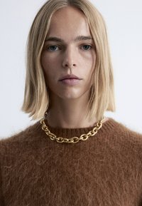 Braunes, fuzzy Sweater mit rundem Ausschnitt, kombiniert mit einer massiven goldenen Kettenschnur, die große, miteinander verbundene Glieder aufweist.
