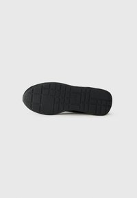 Zwarte rubberen sneakerzool met een gestructureerd profiel. Ronde vorm, vlakke basis en een minimalistisch ontwerp zonder extra kleur of details.