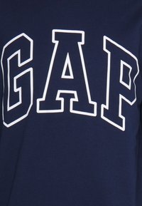 T-shirt en coton bleu marine avec le texte blanc audacieux "GAP" imprimé sur la poitrine, doté d'un col rond classique et d'une texture douce.