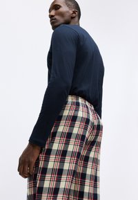Mörkblå skjorta med lång ärm i kombination med rutig pyjamasbyxor i krämfärg, mörkblått och rött. Har elastiskt midjeband och mjukt tyg.