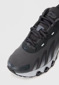 Crne i sive Nike Air Max tenisice s mrežastim gornjim dijelom, crnim vezicama i vidljivim zračnim jastučićima u potplatu, u fokusu na bijeloj pozadini.