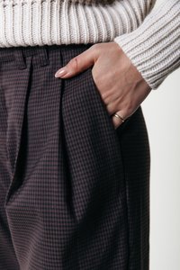 Pantalones de cuadros oscuros con pliegues, que presentan un bolsillo en el lado derecho. La tela tiene una textura suave con un ligero brillo.