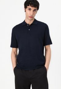 Polo shirt marine avec un col classique, des manches courtes et un plastron à deux boutons ; texture lisse et design ajusté.