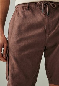 Braune, strukturierte Shorts mit einem elastischen Bund, Kordelzug und seitlichen Taschen. Der Stoff wirkt leicht und lässig.