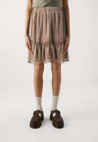 Kort brun skjørt med mønstrete design, volangkant, og elastisk midje, parret med lysebrune tresko og beige sokker.