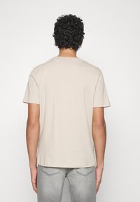 T-shirt in cotone beige con maniche corte e scollo rotondo, caratterizzato da un design semplice e una vestibilità comoda. La vista dal retro mostra una texture liscia.