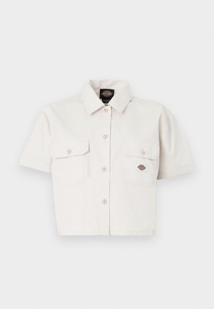 Lühikeste varrukatega, lühikeseks lõigatud valgest puuvillast särk, millel on kaks rinnataskut, nööbid ees ja logopatch vasakus taskus.
