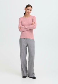 Lys pink ribbet sweater med rund halsudskæring og knapdetaljer, parret med grå ternede vide bukser og sorte sko.