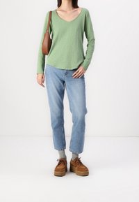 Maglia verde a maniche lunghe con scollo a V, abbinata a jeans a gamba dritta blu chiaro. Le scarpe stringate brown con platform completano l'outfit.