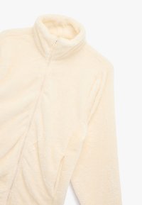 Fleecejacke in Cremefarbe mit hohem Kragen, Reißverschluss vorne, langen Ärmeln und leicht strukturierter Oberfläche. Verfügt über geraffte Details.