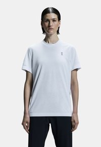 Vit t-shirt med kort ärm, tillverkad av mjukt tyg, med rundad hals och diskret logotyp på bröstet och ärmen.
