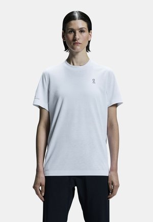 Vit t-shirt med kort ärm, tillverkad av mjukt tyg, med rundad hals och diskret logotyp på bröstet och ärmen.