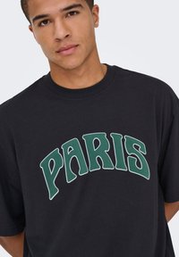 Zwart katoenen T-shirt met een groene gebogen "PARIS" afbeelding. Korte mouwen, ronde hals, relaxte pasvorm, gladde textuur.