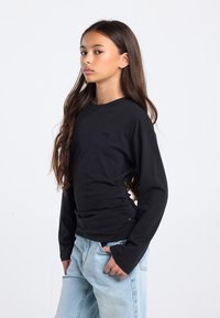 Zwarte T-shirt met lange mouwen van katoen, met een ronde hals en een slanke pasvorm. Gecombineerd met lichtblauwe jeans met een losse pasvorm.