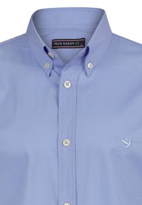 Camisa de botón azul claro con cuello clásico, con botones blancos y un pequeño bordado de un colibrí en el lado izquierdo del pecho.