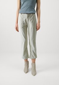 Light green corduroy trousers with a relaxed fit, featuring front pockets and a zipper closure, paired with beige pointed ankle boots.