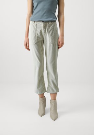 Lys grønne corduroy-bukser med en afslappet pasform, der har forlommer og lynlås, parret med beige spidse ankelstøvler.