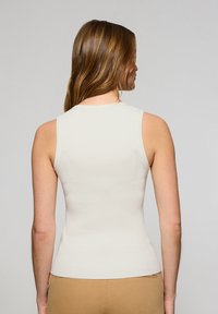 Top senza maniche a coste color crema con un design aderente e scollatura rotonda, che mette in evidenza una texture liscia e linee pulite dalla vista posteriore.