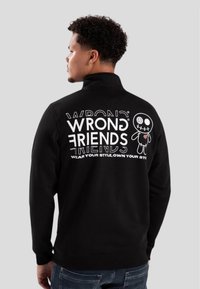 Sudadera negra con el texto gráfico en blanco "WRONG FRIENDS" y un personaje de dibujos animados en la parte posterior. Cuello alto y puños de canalé.