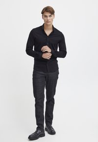 Fekete, hosszú ujjú, gombos ing, slim fit, puha tapintású; sötétszürke nadrággal és fekete slip-on cipővel párosítva, fehér háttér előtt áll.